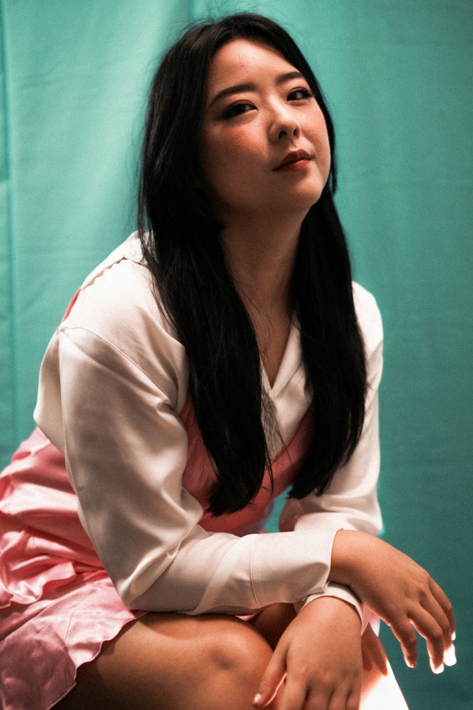 Sam X Wong, a Malaysian Chinese woman, tilts her head slightly back and looks pensively into the camera